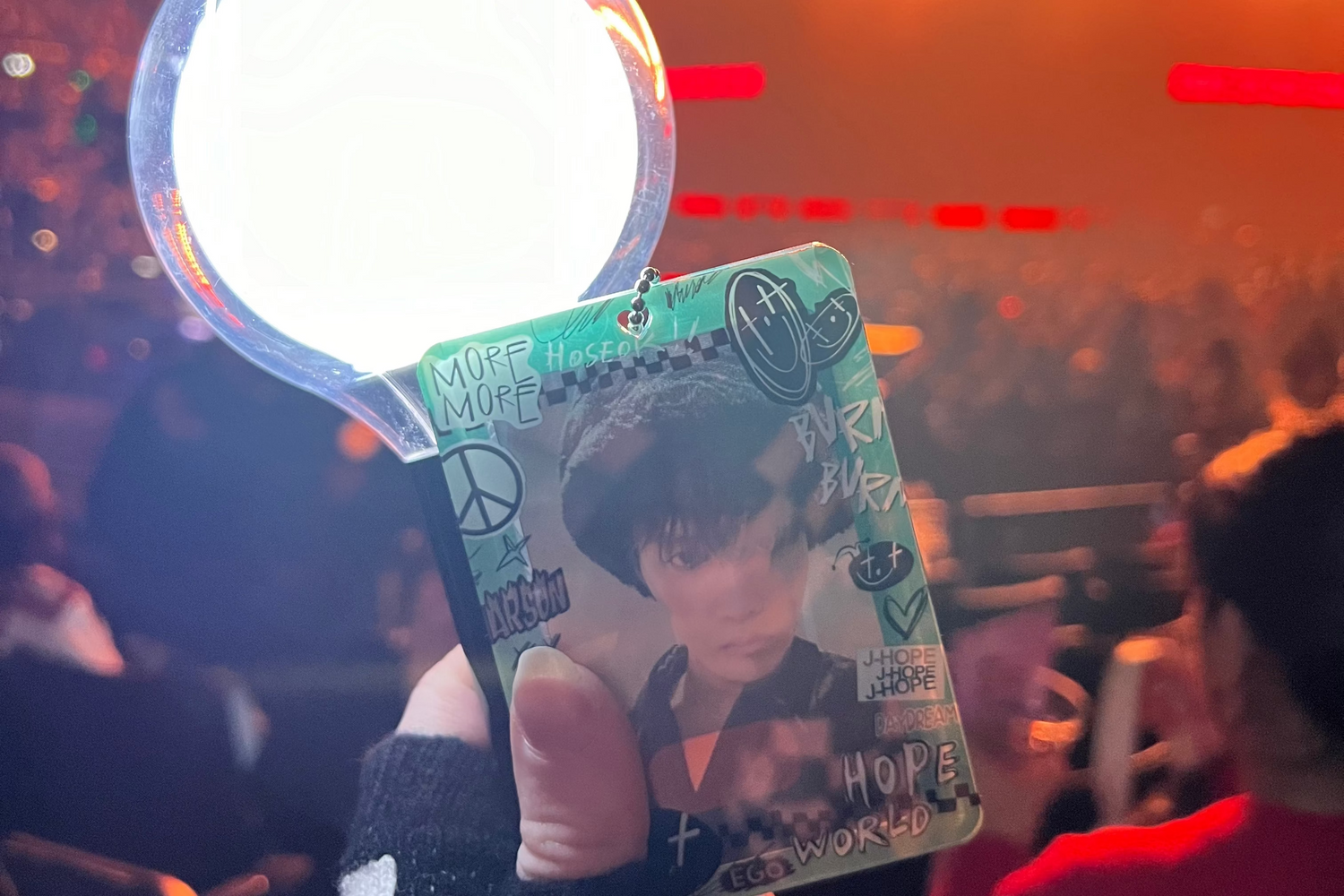 Person holding a card with a person's face at a concert with bright lights and crowd in the background